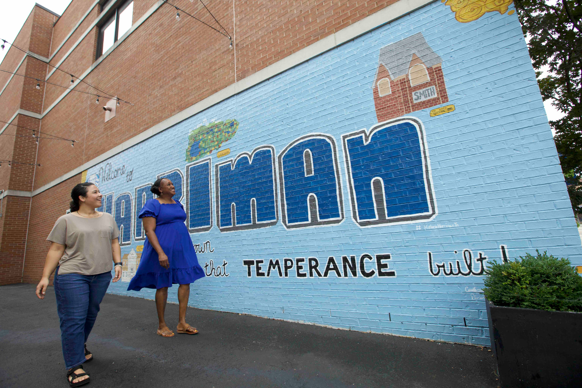 Two people walking past the Welcome to Harriman mural on a brick building