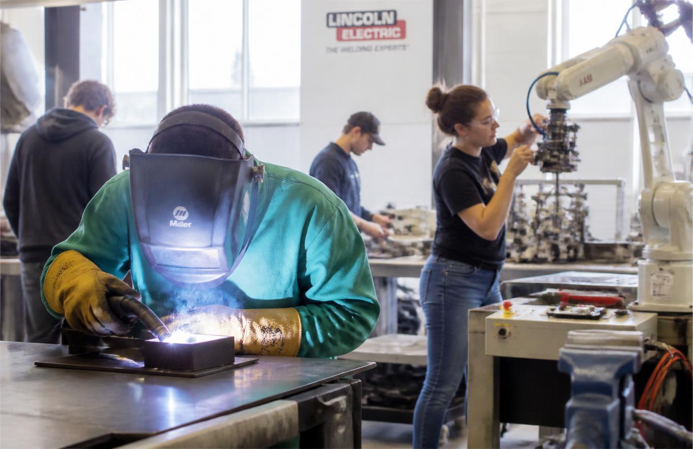 Students welding and operating robotics equipment in a technical training lab